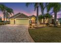 Dusk view of single-Gathering home featuring stone accents, lush landscaping, a paver driveway, and a red front door at 1312 Patrick Pl, The Villages, FL 32162