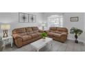 Comfortable living room featuring cozy brown sofas, a modern coffee table, and bright natural light from the sheer curtained windows at 16726 Hidden Spring Dr, Clermont, FL 34714