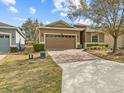 Exterior view of a one-story house with a brick-paver driveway, a two-car garage, and mature trees and shrubs at 3808 Serena Ln, Clermont, FL 34711