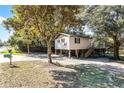 Wide angle exterior of a tan raised stilt home with mature trees in the front yard at 6490 Se 180Th Avenue Rd, Ocklawaha, FL 32179