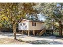 Exterior of a tan raised stilt home with gravel yard, stairs and mature trees at 6490 Se 180Th Avenue Rd, Ocklawaha, FL 32179