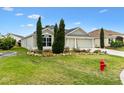 Inviting single-story house featuring a lush green lawn, beautiful landscaping with mature trees and a three-car garage at 3233 Belcherry Loop, The Villages, FL 32163