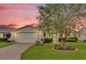 Charming home at sunset with a well-manicured lawn and a beautiful tree in the front yard at 1106 Blythe Way, The Villages, FL 32162