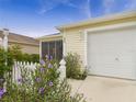 The home's exterior featuring a white garage door, light fixture, and pretty purple flowers at 620 Vagabond St, The Villages, FL 32163