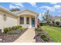 Home exterior showcasing a tiled walkway to a decorative blue front door flanked by flowering plants and bright green grass at 5370 Indian Ocean Loop, Tavares, FL 32778