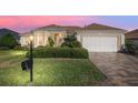Charming single-story home featuring a well-manicured lawn, a two-car garage and tropical landscaping at dusk at 12239 Se 92Nd Court Rd, Summerfield, FL 34491