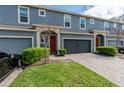 Exterior view of blue townhomes featuring a paver driveway, garages, manicured landscaping and red front doors at 384 Coral Beach Cir, Casselberry, FL 32707