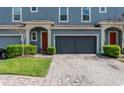 Exterior view of blue townhomes featuring a paver driveway, garages, manicured landscaping and red front doors at 384 Coral Beach Cir, Casselberry, FL 32707