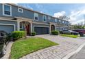 Exterior view of blue townhomes featuring a paver driveway, garages, manicured landscaping and red front doors at 384 Coral Beach Cir, Casselberry, FL 32707