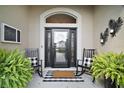 Charming front porch featuring rocking chairs, decorative plants, and a stylish front door with glass panels at 3426 Boardroom Trl, The Villages, FL 32163