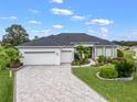 Landscaped front yard with a paver driveway leading to a three-car garage, and a beautifully maintained lawn at 17126 Se 117Th Cir, Summerfield, FL 34491