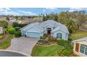 An aerial view of a beautifully landscaped home with a three-car garage, green lawn, and a inviting red front door at 589 Society Hill Cir, The Villages, FL 32162