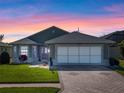 Charming single-story home featuring a brick driveway, two-car garage, manicured lawn, under a stunning sunset at 5718 Illumination Ln, Leesburg, FL 34748