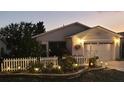 Charming home exterior features a white picket fence, manicured landscaping, and a well-maintained driveway at dusk at 2058 Thornton Ter, The Villages, FL 32162