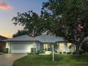 Beautiful single-story home at dusk, featuring a manicured lawn, mature tree, and attached two-car garage at 26821 Augusta Springs Cir, Leesburg, FL 34748