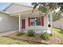 Close-up of a charming covered front porch with a red door and decorative rock landscaping at 2082 Harston Trl, The Villages, FL 32162