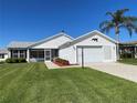 Charming single-story home featuring a well-maintained lawn, mature landscaping, and an attached garage with a decorative accent at 2189 Broxton Pl, The Villages, FL 32162