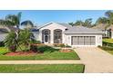 Inviting single-story home with a well-manicured lawn, mature palms, a three-car garage, and a screened front entry at 27023 Old English Ct, Leesburg, FL 34748