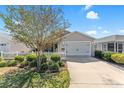 The front exterior showcasing a two-car garage, white picket fence, shrubs, and a concrete driveway at 2602 Young Ln, The Villages, FL 32163