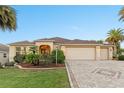 Charming single-story home with a three-car garage, lush landscaping, and a brick-paved driveway at 2428 Maverick Way, The Villages, FL 32162