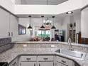Open kitchen view showcasing granite countertops, stainless steel sink, pendant lighting, and access to the living area at 26032 Newcombe Cir, Leesburg, FL 34748