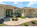 Beautiful home showcasing a beige exterior, green front door, manicured landscaping, and paver walkway at 630 Laurel Run, The Villages, FL 32162