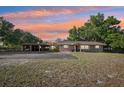 Charming single-story home at sunset featuring a large driveway, well-manicured lawn, and mature shade trees at 23519 State Road 44, Eustis, FL 32736
