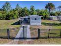Gated single-story home with a covered porch, surrounded by mature trees and a fenced yard at 8901 Se 144Th Ln, Summerfield, FL 34491
