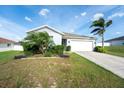 Well-maintained single-Gathering home featuring a two-car garage, green lawn, and tropical landscaping at 2256 Gladiolus Ln, Mascotte, FL 34753