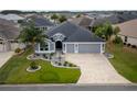 Overhead view of a gray home with a three-car garage, surrounded by green lawns, landscaping, and mature palm trees at 3942 Zenith Loop, The Villages, FL 32163