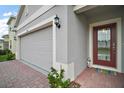 A gray stucco home with a brick walkway leading to a red front door and a two car garage at 444 Shadow Gorge Way, Eustis, FL 32736