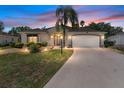 Inviting home exterior illuminated by landscape and sconce lighting at twilight, highlighting the driveway and manicured lawn at 2461 Merida Cir, The Villages, FL 32162