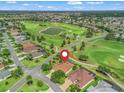 Aerial view showcases a home on a golf course with a pin; scenic community featuring lush greenery and a tranquil lake at 383 Kilmer Way, The Villages, FL 32162