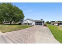 Charming home features a well-maintained lawn, a long brick driveway, and a screened-in porch at 705 Prado Dr, The Villages, FL 32159