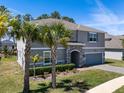 Two-story home featuring a gray exterior with stone accents, blue shutters, and palm trees enhancing curb appeal at 524 Avila Pl, Howey In The Hills, FL 34737