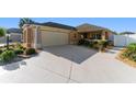 Charming home featuring a well-manicured lawn, neutral stucco, and a two-car garage with an extended, patterned concrete driveway at 648 Mission Hills Trl, The Villages, FL 32162