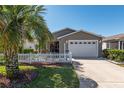 Charming single story home featuring a white picket fence, well-manicured lawn, and a driveway leading to the garage at 992 Pinewood Pl, The Villages, FL 32162