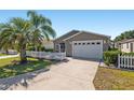 Charming single story home featuring a white picket fence, well-manicured lawn, and a driveway leading to the garage at 992 Pinewood Pl, The Villages, FL 32162