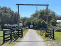 Long driveway leads to the home with a grand wooden archway, fenced perimeter, and lush greenery on either side at 1650 Sundance Dr, St Cloud, FL 34771
