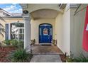Inviting entryway featuring a blue front door with decorative wreath, lush plantings and brick walkway at 848 Hawk Lndg, Fruitland Park, FL 34731