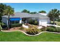 Beautifully landscaped home featuring lush green lawn, a blue awning, palm trees and a brick paved driveway at 3614 Auburndale Ave, The Villages, FL 32162