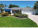 Beautiful home with well-kept lawn, palm trees, blue awning and brick driveway in a pristine community at 3614 Auburndale Ave, The Villages, FL 32162