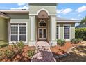 Inviting entryway featuring double doors, decorative columns, and a brick-paved walkway surrounded by landscaped gardens at 38420 Langlois Pl, Leesburg, FL 34788