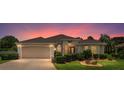 Inviting single-story home with a two-car garage, lush landscaping, and warm exterior lighting at dusk at 1875 Saybrook Way, The Villages, FL 32162