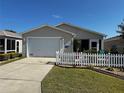 Well-maintained one story home featuring a garage, manicured lawn, and white picket fence at 2449 Kingstree Pl, The Villages, FL 32162
