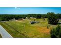 An aerial view of a modest home on a large grassy lot surrounded by lush greenery and a road at 7701 Groveland Farms Rd, Groveland, FL 34736