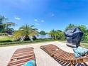 Relaxing backyard patio with lake view, lounge chairs, covered grill, and lush tropical landscaping at 8387 Bridgeport Bay Cir, Mount Dora, FL 32757