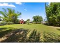 Large, green backyard with mature trees and landscaping, plus a charming red barn at the edge of the property at 28924 Discovery Rd, Tavares, FL 32778