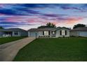 Cozy single-story home featuring a well-kept lawn, paved driveway, and charming curb appeal at sunset at 3590 Auburndale Ave, The Villages, FL 32162