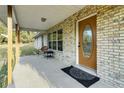Covered front porch features a brick facade, stained front door, and outdoor seating with a welcome mat at 9236 County Road 48, Yalaha, FL 34797